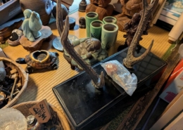 神奈川県横浜市青葉区の実家片付けで見つかった鹿角の刀掛け。黒塗りの台座に天然鹿角が立てられ、周囲には布袋像や木彫七福神、青磁の筆筒など多彩な骨董品が並ぶ温かな和室の光景。