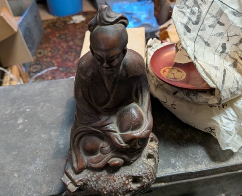 神奈川県伊勢原市大住台の空き家片付けで見つかった古備前の賢人像。深い表情で坐す人物像を鑑定士が正面から確認している様子。焼締めの土味と自然な焼色が残る骨董陶磁器。