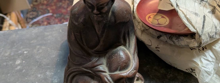 神奈川県伊勢原市大住台の空き家片付けで見つかった古備前の賢人像。深い表情で坐す人物像を鑑定士が正面から確認している様子。焼締めの土味と自然な焼色が残る骨董陶磁器。