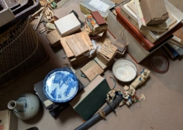空き家となった実家の片付け中に見つかった明治時代の骨董品。木箱入りの書道具、和本、染付の皿、陶器、刀剣などが床に広げられている様子。
